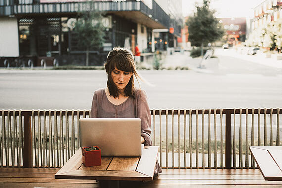 Eine Frau sitzt draußen mit Laptop an einem Tisch.